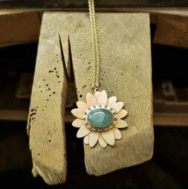 image of a gold daisy necklace with an aquamarine and champagne diamonds on a benchpeg