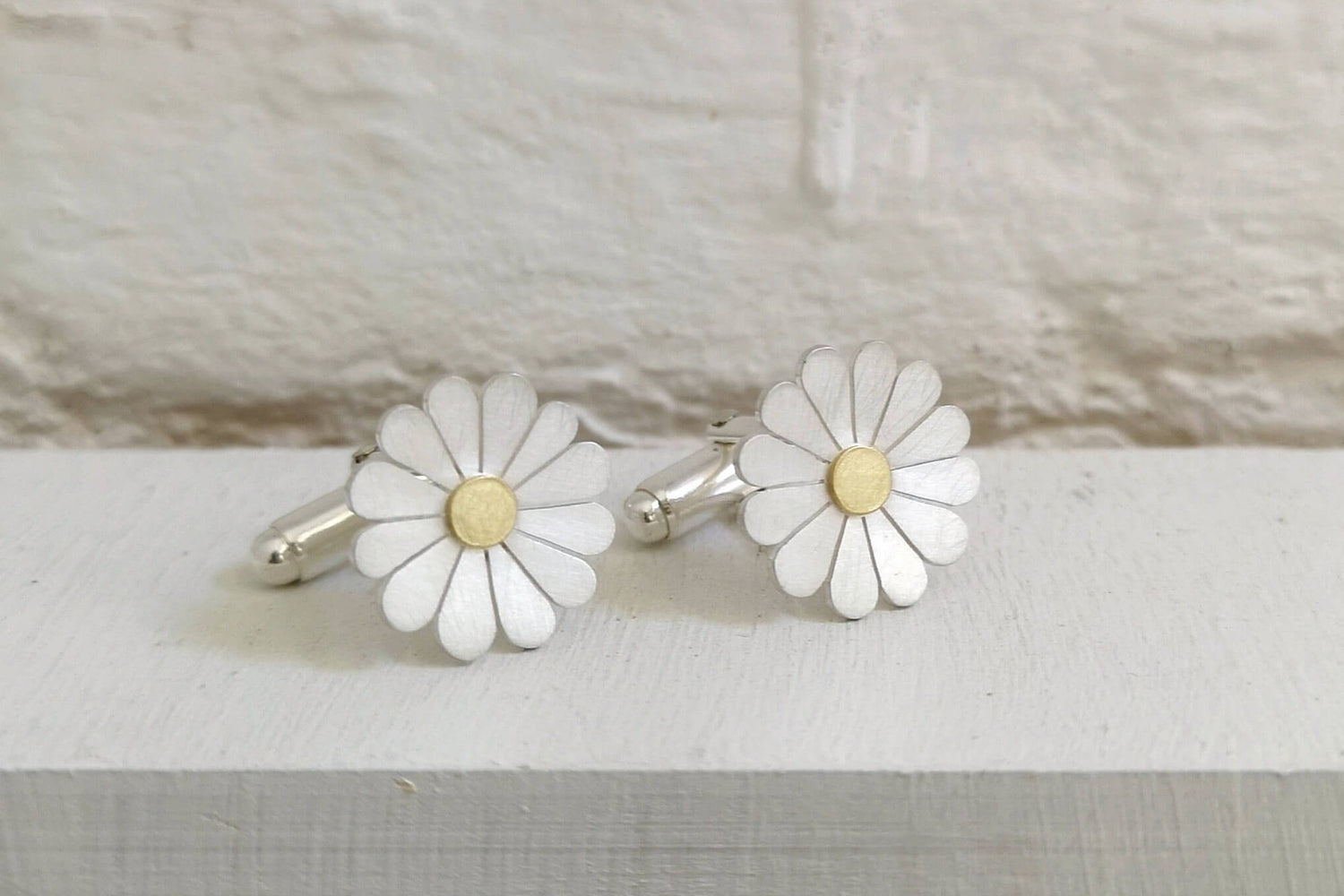 silver and gold daisy cufflinks on a white background