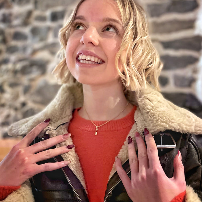 Girl in an orange sweater wearing a mini gold ice skate blade necklace