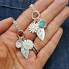 Silver necklace with floral and leaf charms held in a hand against a denim background