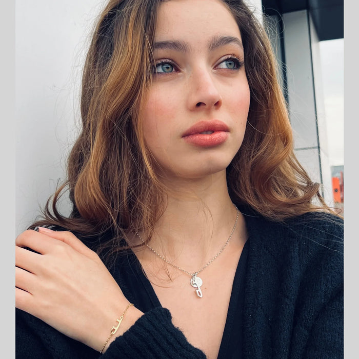 Woman wearing a black top, silver ice skate blade necklace and gold bracelet with a neutral background