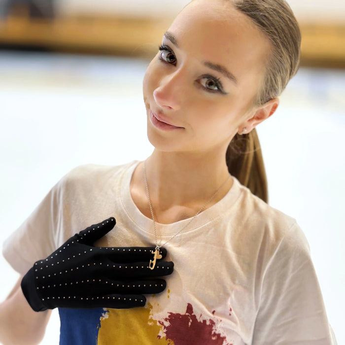 female figure skater in a colourful top on ice showing her necklace which features a silver ice blade and a heart charm