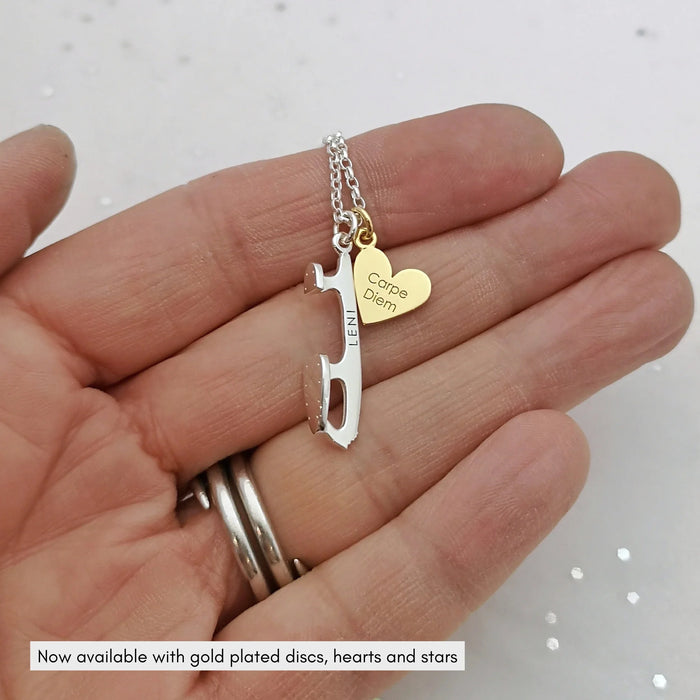 hand holding a personalised silver ice skate blade necklace with a personalised gold plated heart charm