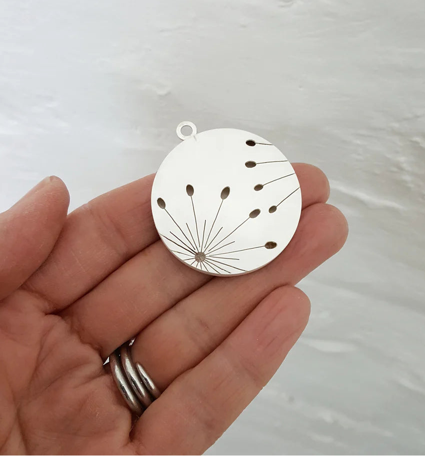 Silver pendant held in a hand against a light background