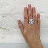 Hand wearing a silver ring with floral design on a light gray background
