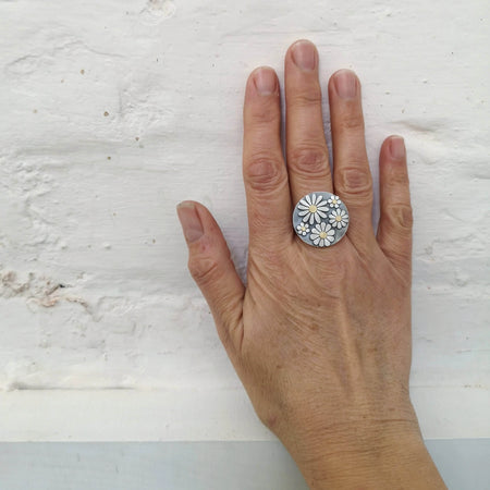 Hand wearing a silver ring with floral design on a light gray background