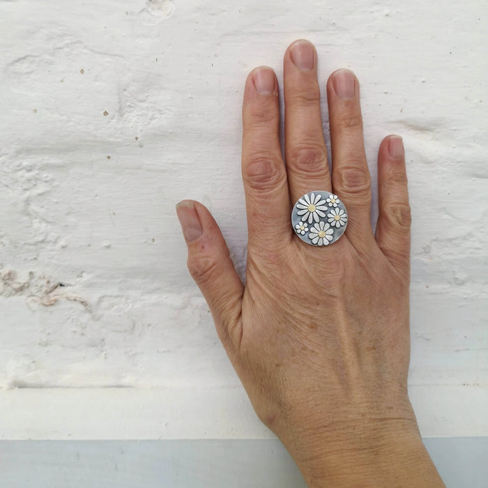 Hand wearing a silver ring with floral design on a light gray background