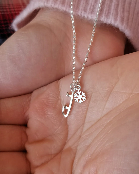 girl in a pink sweater holding a silver necklace with an ice skate blade and a snowflake charm in her hands