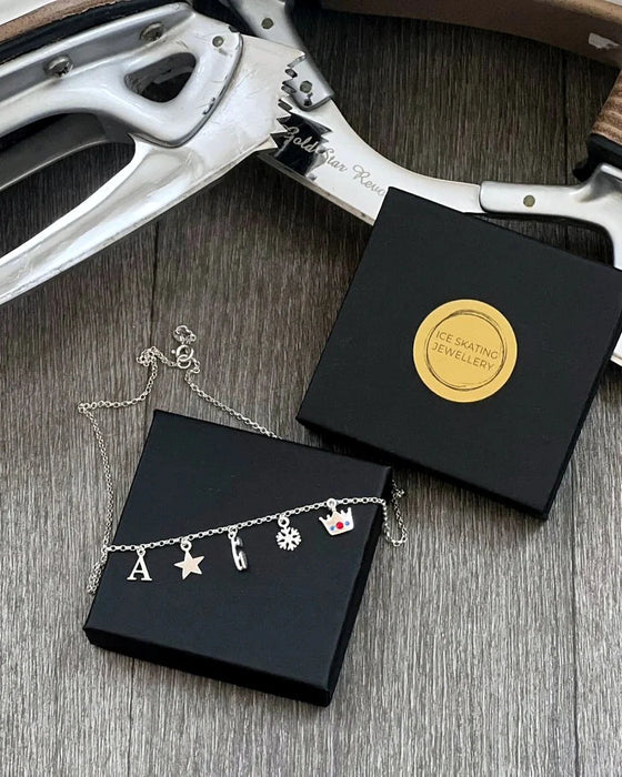 close up of a silver charm necklace on a presentation box with ice skates in the background
