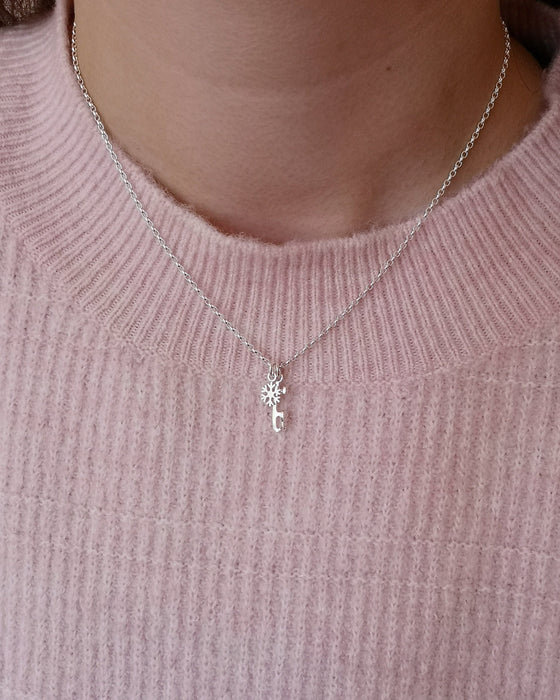 girl in a pink sweater wearing a silver necklace with an ice skate blade and a snowflake charm