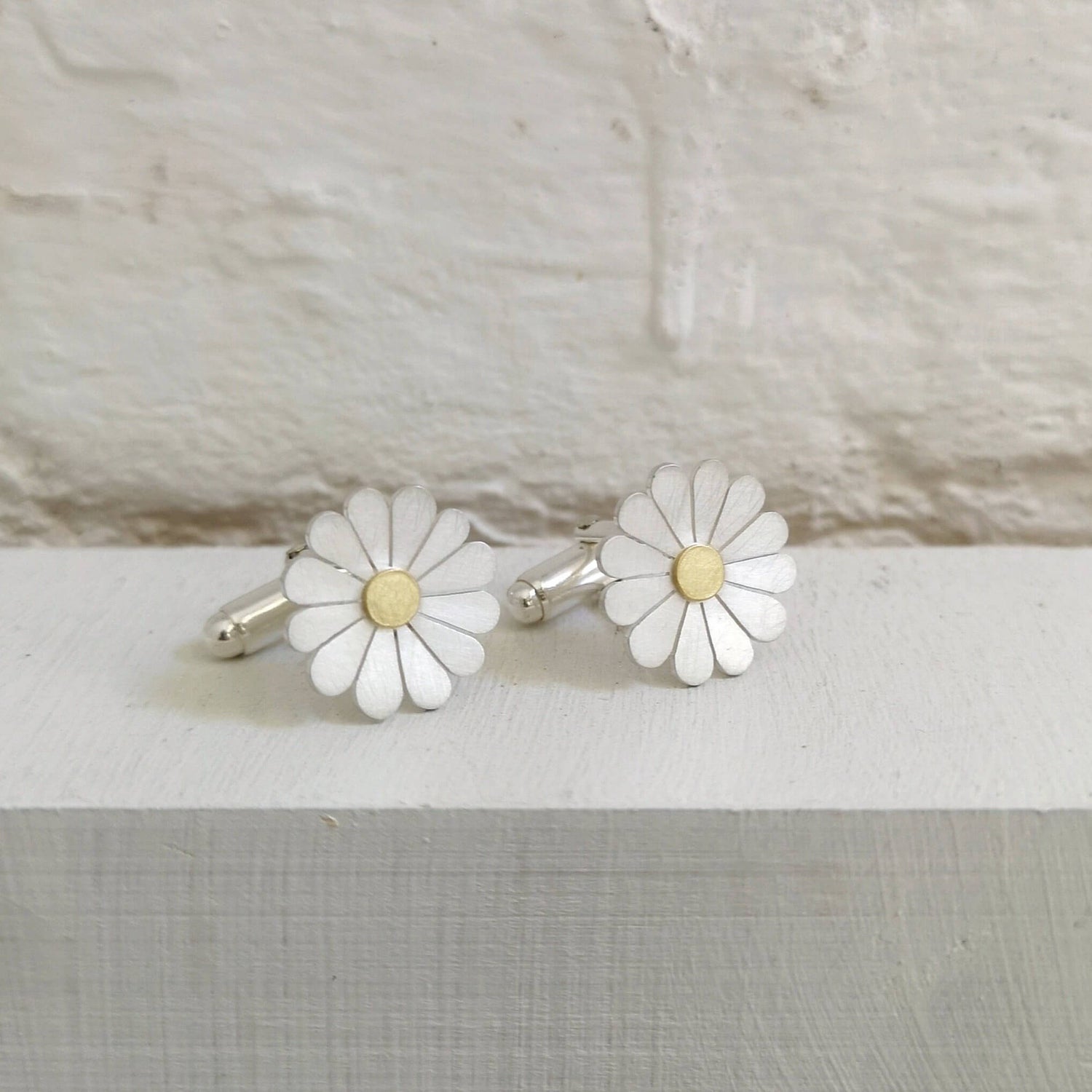 silver and gold daisy cufflinks on a white background