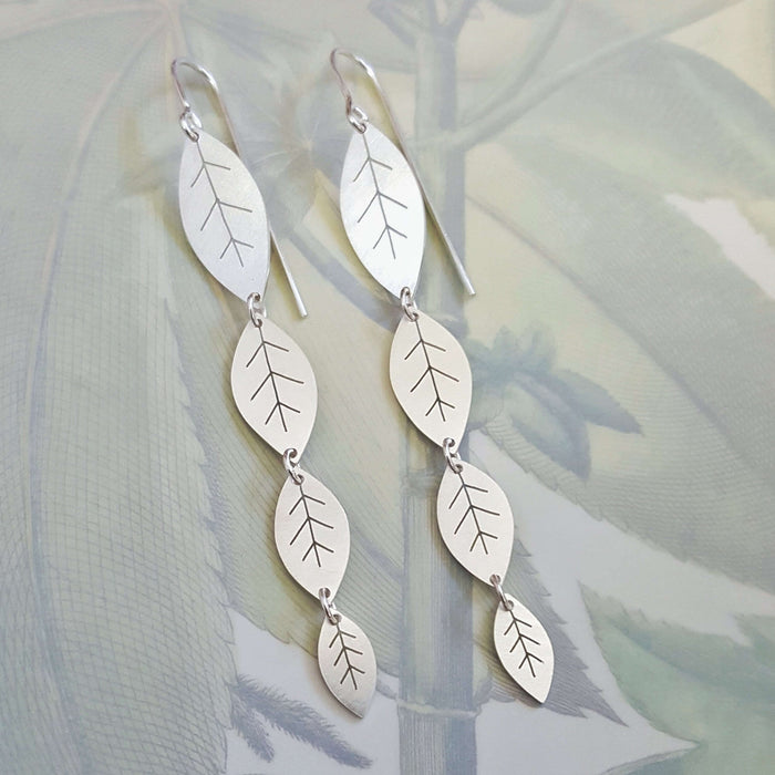 Silver leaf-shaped earrings on a soft green background